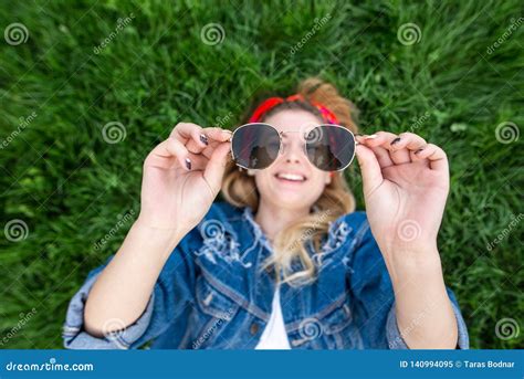 Happy Girl Lying On Green Grass Holding Sunglasses In Her Hands Looking At Camera And Smiling