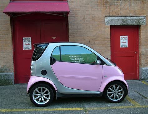 a pink and silver smart car parked in front of a brick building with ...