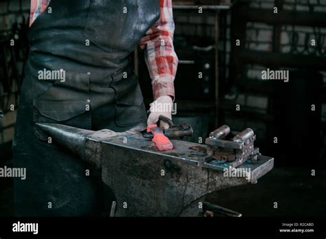 Blacksmith Working With Red Hot Metal Workpiece Of New Hammer At Anvil In A Forge Stock Photo