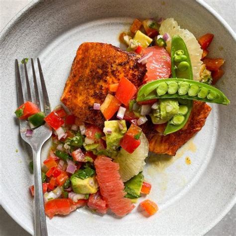 A White Plate Topped With Fish And Veggies Next To A Knife And Fork