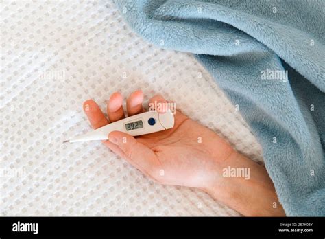 Closeup Of Man Hand Holding A Digital Thermometer Lying On The Bed