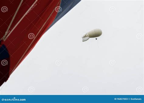 White Coloured Blimp, Hot Air Airship in Grey Sky in Rainy Day Nearby with Vivid Red Hot Air ...