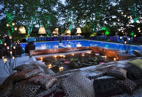 An Outdoor Pool With Candles Lit Up In The Background And Pillows On