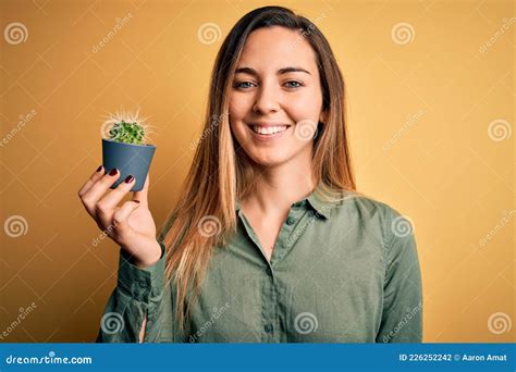 Jeune Belle Femme Blonde Aux Yeux Bleus Tenant Un Petit Pot De Cactus Sur Fond Jaune Avec Un