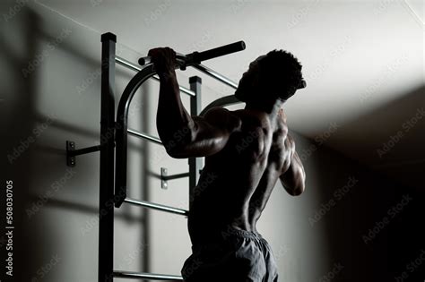 African American Man With Naked Torso Pulls Up On Horizontal Bar In Gym