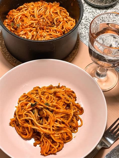 A White Plate Topped With Spaghetti Next To A Pot Of Pasta And Glasses