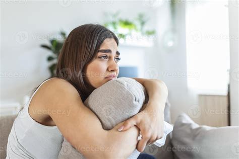 mujer joven abrazando la almohada con depresión y llorando en el sofá