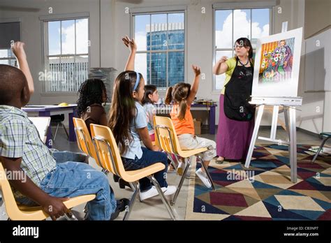 An art teacher standing by easel teaching her young students in art ...