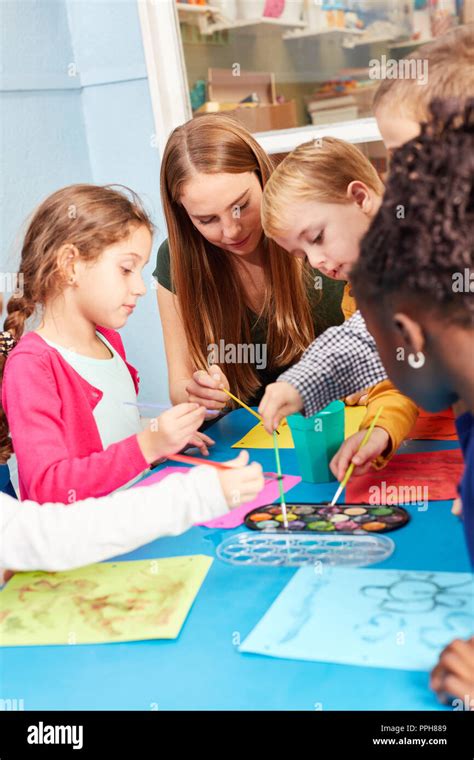 Los Niños Pintando En La Pintura Con Acuarela Y Pincel De Clase Supervisado Por Una Maestra De