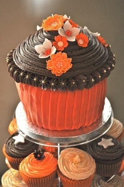 A Three Tiered Cake With Orange Frosting And Flowers On Top Surrounded