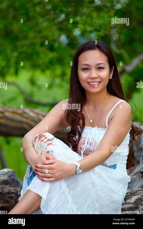 Full Body Adult Filipino Female In Dress Looking At Camera While Relaxing On Trunk Of Tree On