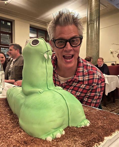 A Man Sitting In Front Of A Cake Shaped Like A Green Creature With