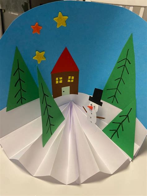 An Origami Snowman With A House And Trees In The Background On A Paper