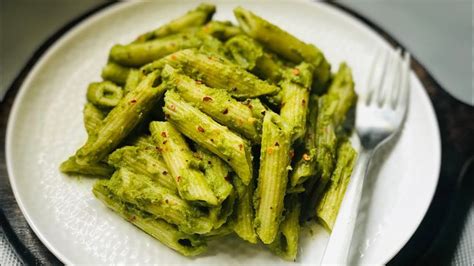 A White Plate Topped With Green Pasta Covered In Pesto Sauce And A