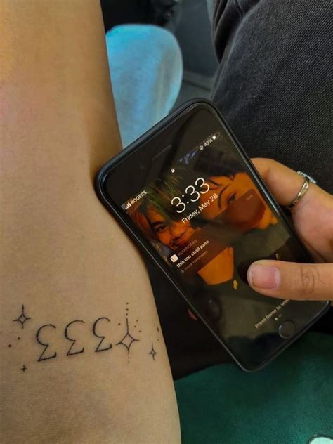 A Person With A Tattoo On Their Arm Holding A Cell Phone