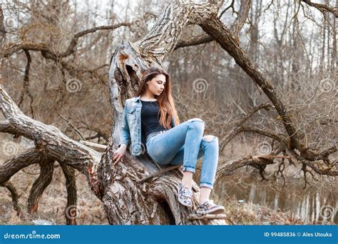 Beautiful Girl In Jeans Jacket And Denim Shorts Sitting On A Tree