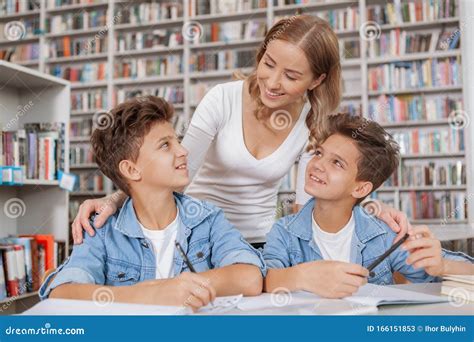 Happy Mother Helping Her Twin Sons With Studying At The Library Stock