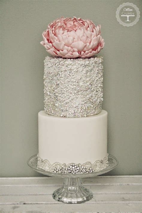 A Three Tiered Wedding Cake With A Pink Flower On Top And Silver Sequins