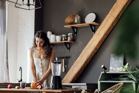 Charming Curly Haired Brunette Girl In Linen Sundress Prepares Fruit Smoothie In Blender In