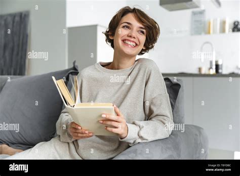 Happy Young Woman Sitting On A Couch At Home Reading A Book Stock