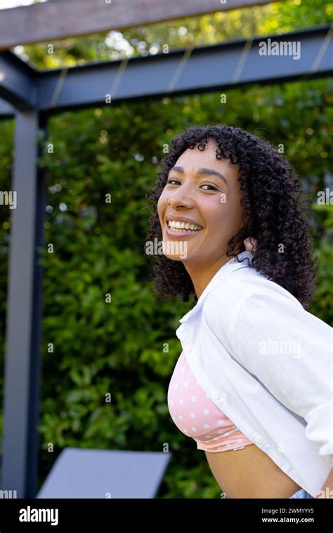 Young Biracial Woman With Curly Hair Smiles Brightly Wearing A Pink