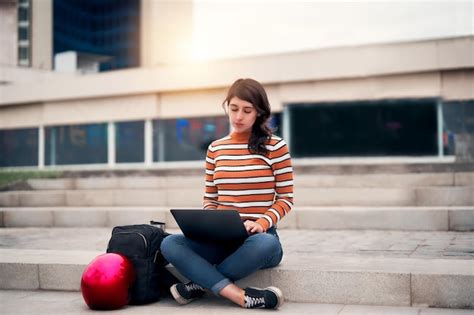 Mujer joven latina sentada al aire libre en las escaleras con una computadora portátil y una