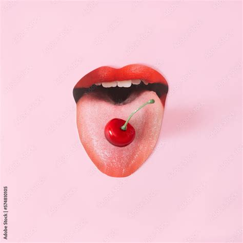 A wide open women's mouth with red lips and a cherry on the tongue. Pink background. Minimal ...