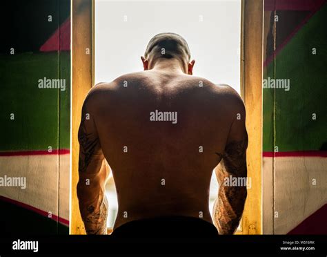 Portrait Of Muscular Man With Nude Torso And Tattoos On Arms Standing Near Window Looking