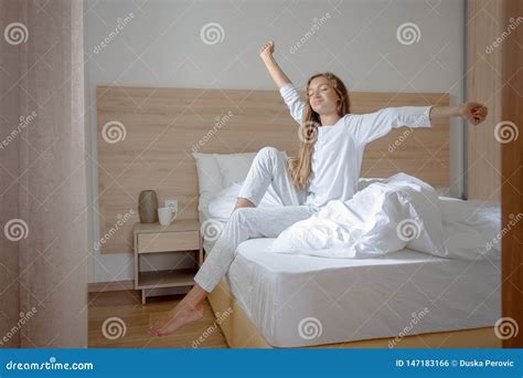 Young Woman Waking Up In Her Bedroom Sitting On The Bed Stretching