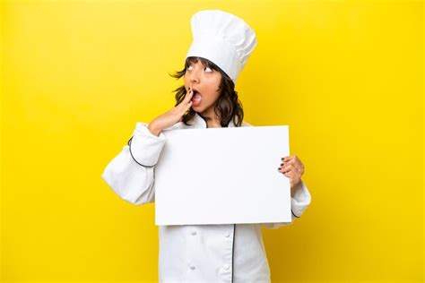 Joven chef mujer latina aislada de fondo amarillo sosteniendo un cartel vacío con expresión
