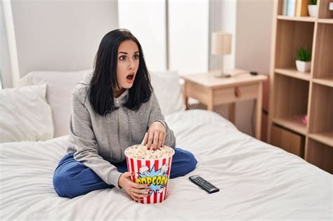 Hispanic Woman Eating Popcorn Watching A Movie On The Bed In Shock Face