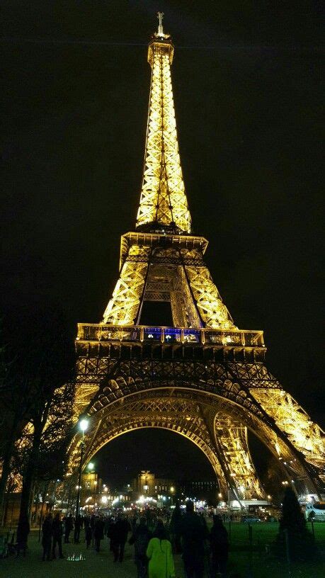 the eiffel tower lit up at night with people walking around in front of it