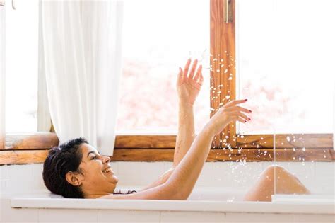 Mulher latina de meia idade tomando banho feliz e sorrindo diversão e prazer na banheira