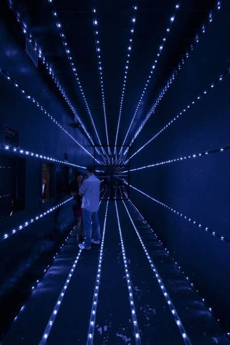 Two People Walking Through A Tunnel With Blue Lights On The Walls And