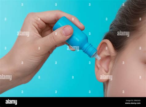 Mother Dripping Medication Into Daughters Ear On Light Blue Background