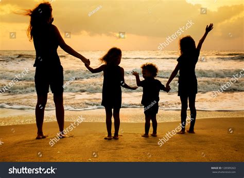 Mother And Three Kids Silhouettes Standing On Beach At Sunset Stock