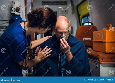 Woman In Medical Uniform Stands With Man Who Sits In Oxygen Mask In