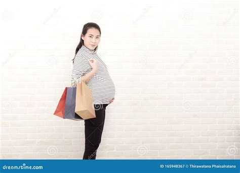 Pregnant Mother Holds A Shopping Bag On A White Brick Background Asian Pregnant Woman Stand And