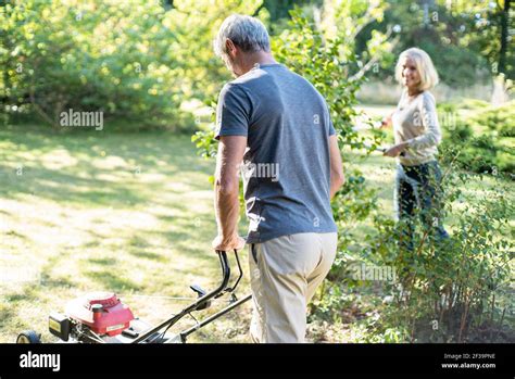 Mature Man Mowing Lawn In Backyard While His Wife Working In Background Stock Photo Alamy