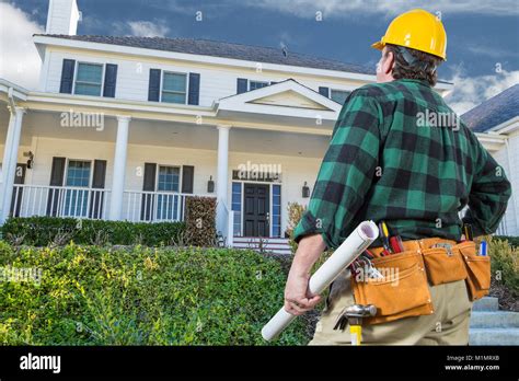 Male Contractor With Hard Hat And Tool Belt Looking At Custom House