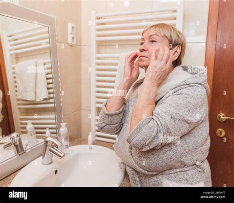 Senior Woman In Bathrobe Touching Her Soft Face Skin And Does Massage