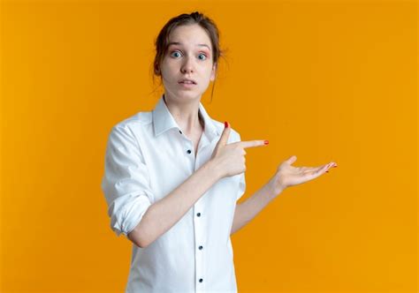Jeune fille russe blonde surprise points à la main vide isolé sur l espace orange avec copie