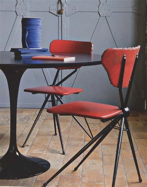 Three Red Chairs Sitting At A Black Table With Two Blue Vases On Top Of It