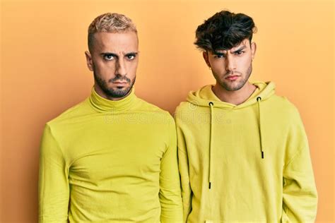 Homosexual Gay Couple Standing Together Wearing Yellow Clothes Skeptic And Nervous Frowning