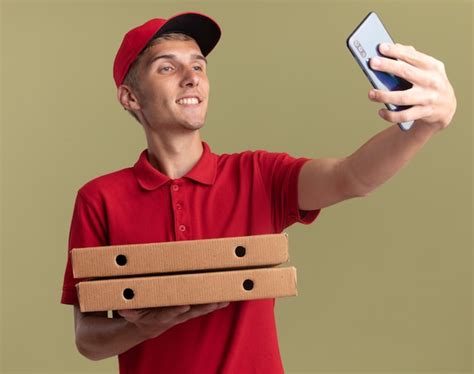 Un Jeune Livreur Blond Souriant Tient Des Boîtes à Pizza Et Regarde Le