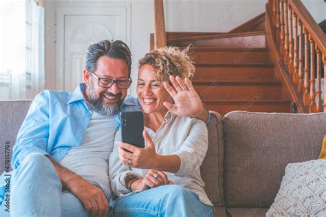 Happy Caucasian Couple Resting On Sofa Waving Hand In Hello Gesture