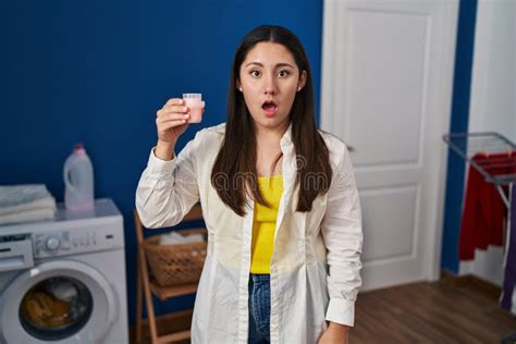 Jovem Latina Lavando Roupa Segurando Detergente Assustada E Surpreendida Boca Aberta Para