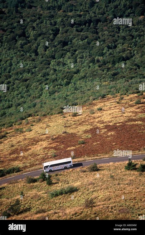 Tour Bus Driving On Curved Road Through Volcanic Landscape Below Puy De