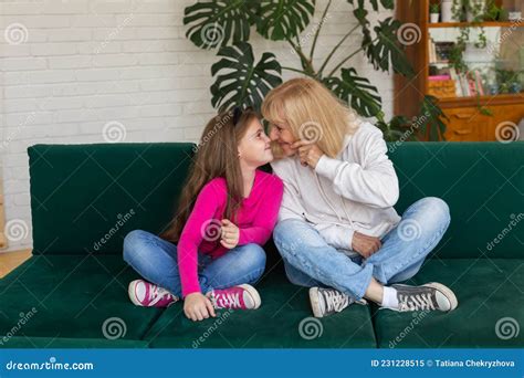 Happy Granddaughter And Grandmother Sitting On Sofa In Funny Pose