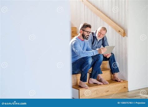 An Adult Son And Senior Father With Tablet Sitting On Stairs Indoors At